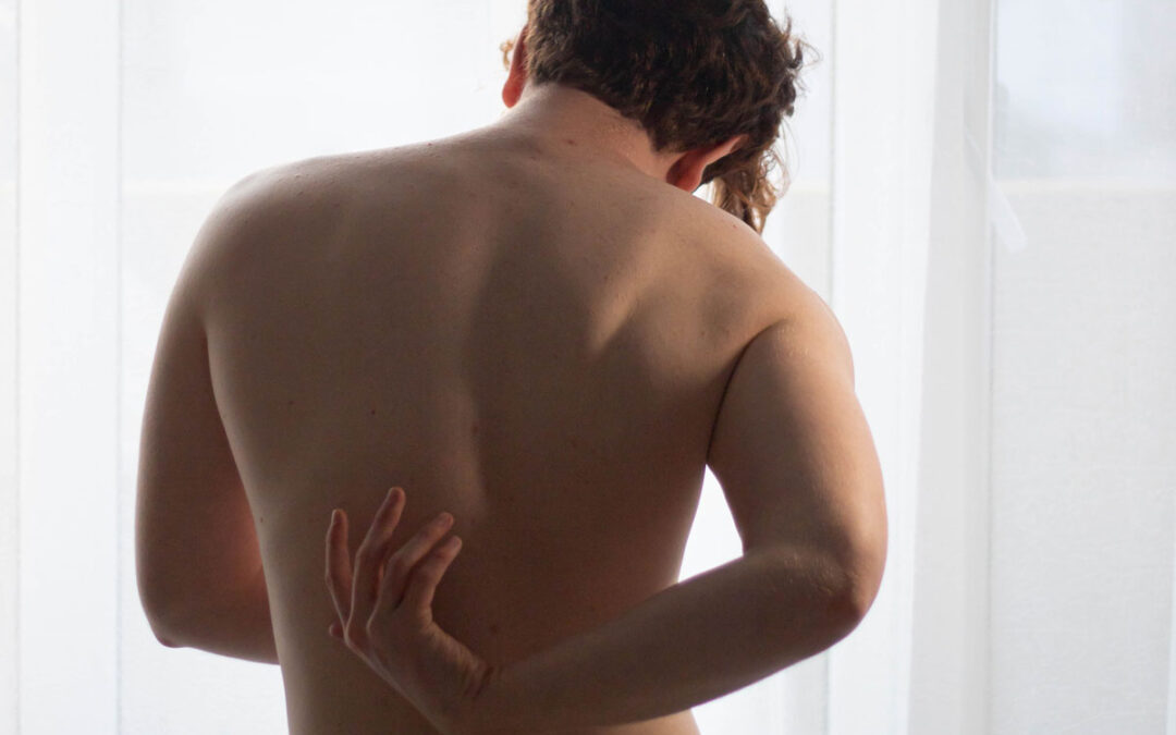 Mensch mit nacktem Oberkörper fasst sich an den Rücken.